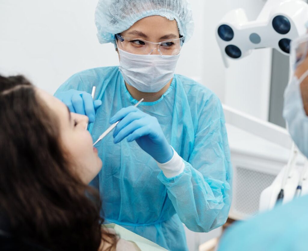 Woman in Blue Long Sleeve Scrub Suit Checking the Patient's Teeth
